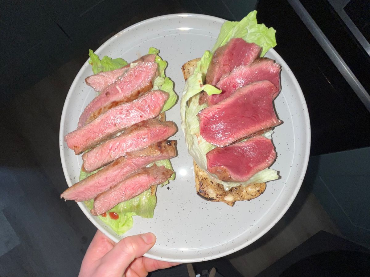 Two open steak sandwiches with sliced rare steak and lettuce on toasted bread