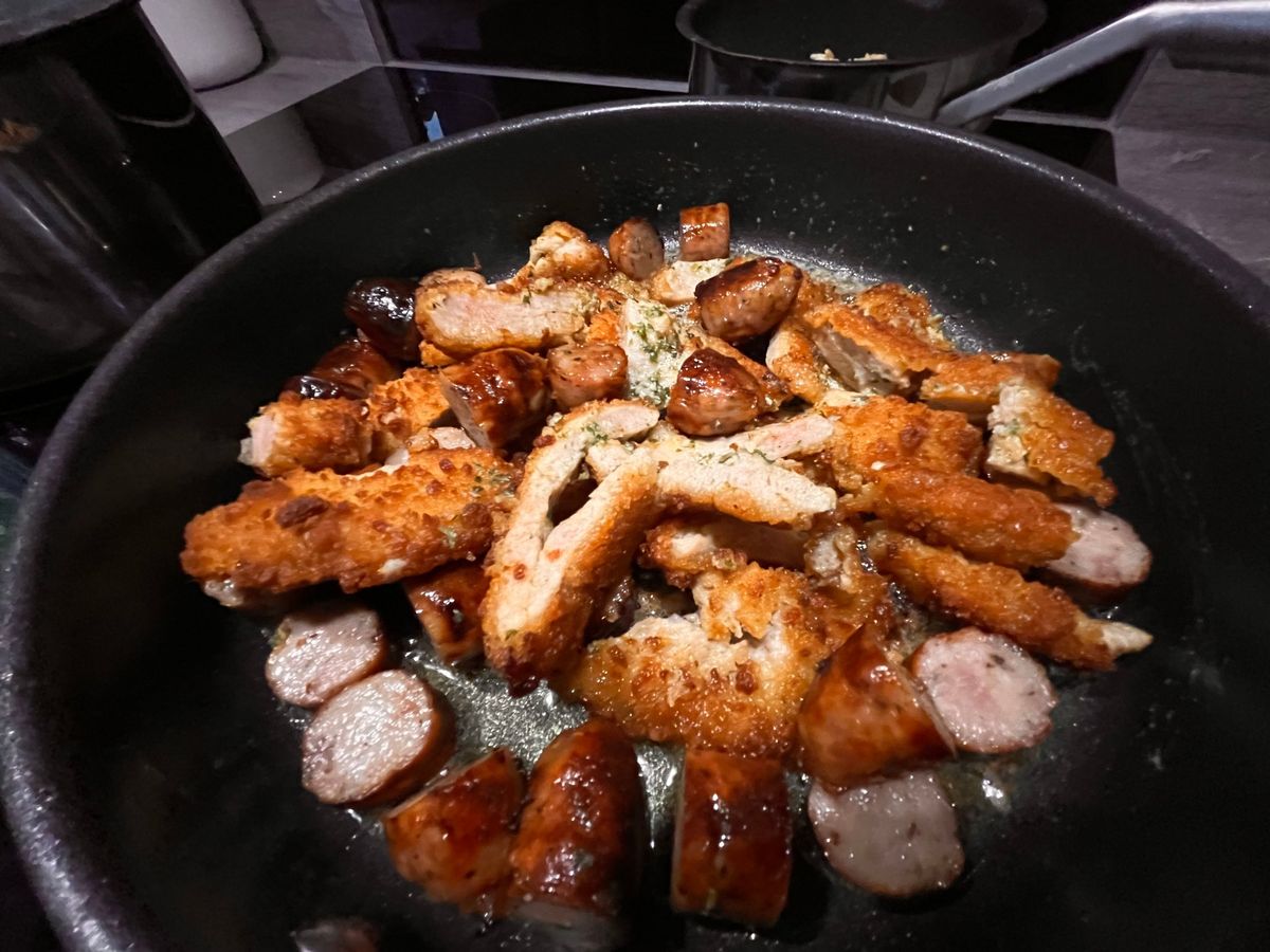Sliced sausages and golden breaded pork pieces frying in a pan