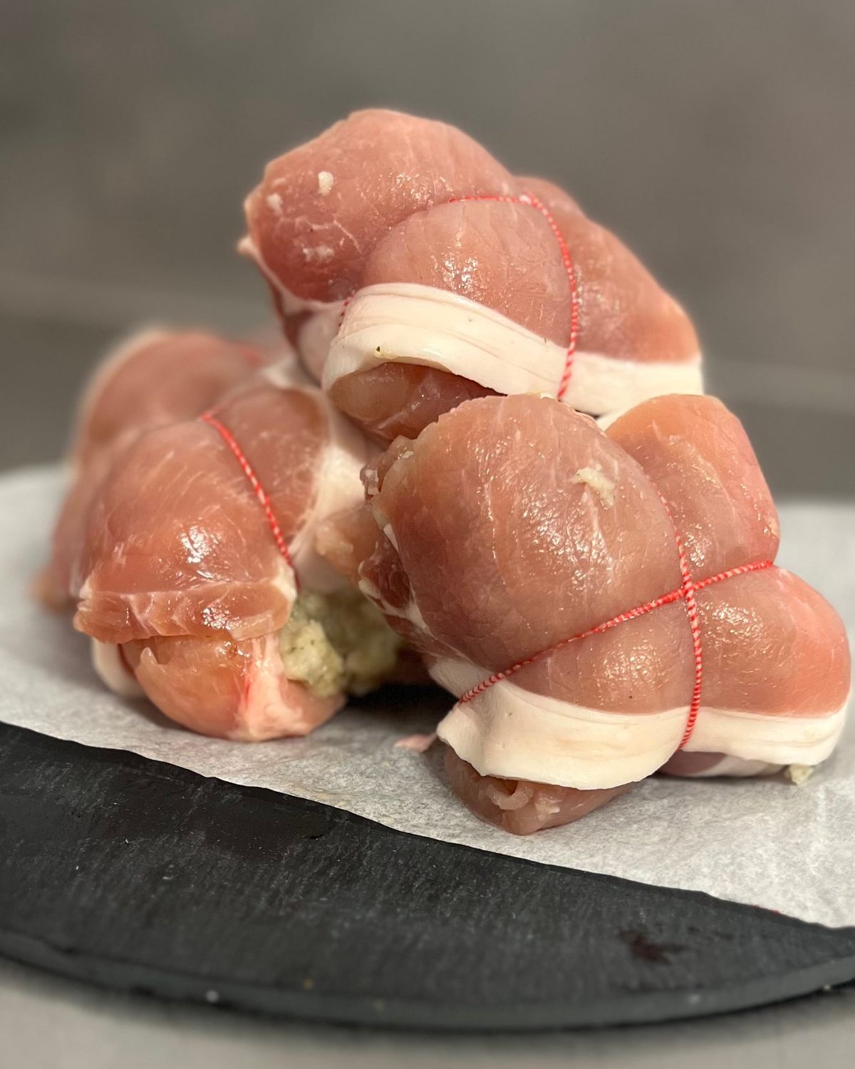 Stuffed and tied pork rolls wrapped in fat and red string, on a slate board